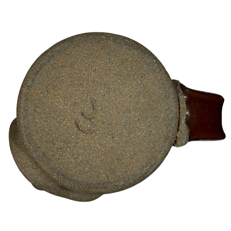 Bottom view of an ugly face pottery vintage winking mug showing textured base and brown handle