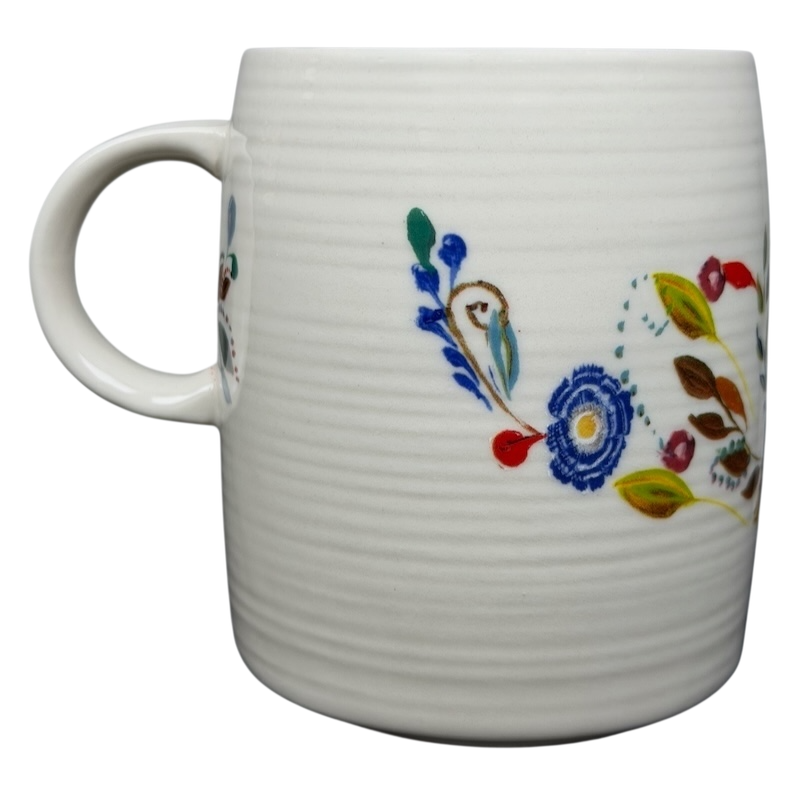 Anthropologie J monogram Starla Halfmann mug with colorful floral designs on a textured white background
