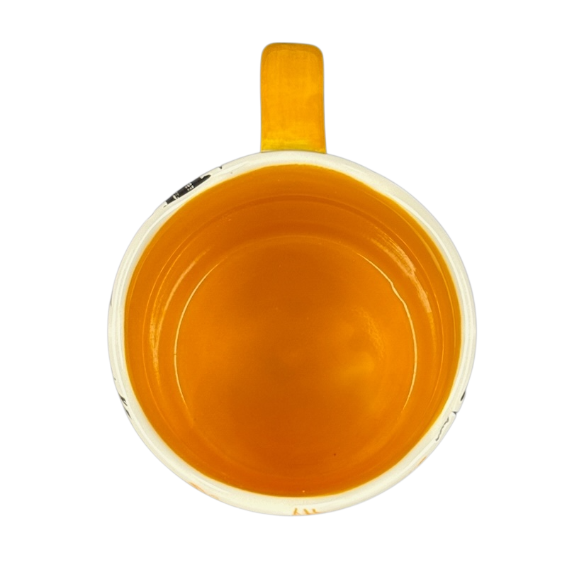 Top view of empty orange glazed ceramic mug with yellow handle on black background Angela Staehling Halloween collectible mug