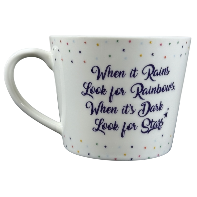 Cooksmart When It Rains Look For Rainbows mug. white ceramic with purple script quote and multicolor star pattern