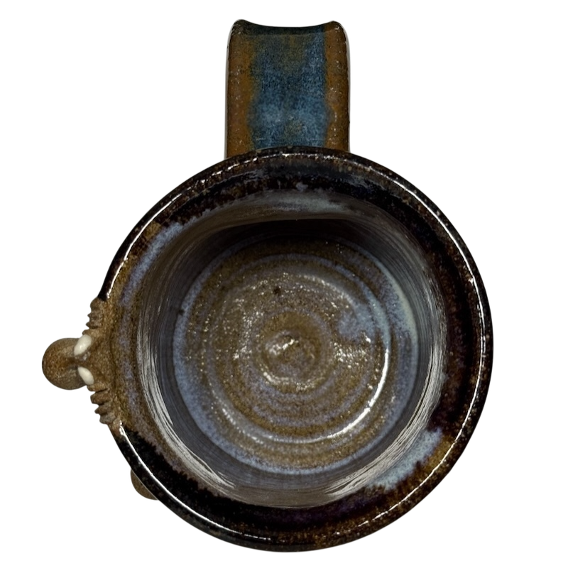 Top view of ugly face pottery vintage winking mug with earthy brown and blue glaze