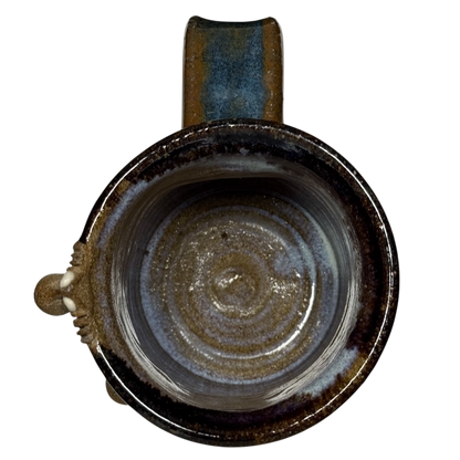 Top view of ugly face pottery vintage winking mug with earthy brown and blue glaze